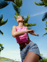 A woman leaps into the air, clutching a frisbee, with a palm tree and clear blue sky serving as the...