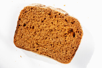 Slice of fresh dark bread on white background in sunlight