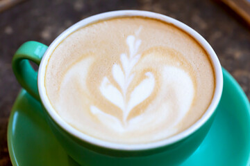 Fresh tasty aromatic coffee latte with foam and pattern in green cup on table close-up. Delicious breakfast. Selective focus