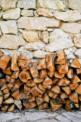 Stack of firewood is stacked against the stone wall of a house on a paved path