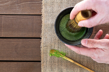 man preparing matcha tea with bamboo whisk at wooden table, top view