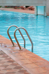 Grab bars ladder in the blue swimming pool. Stainless steel swimming pool ladder.
