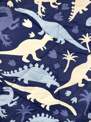 Close up of kids bed linen fabric in dinosaur shape and other grass and palm pattern. In shades of blue, dark blue, light blue, and white color. Kids cute fabric textile. Seamless background texture