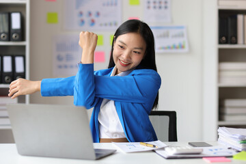 Businesswoman working on computer at office. She was stretching to relieve herself from sitting in an office chair for a long time.