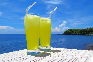 Two bright yellow lemon pineapple tropical drinks. Blue sunny sky with clouds, calm water, romantic...