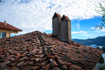 Naklejka premium View of an old roof covered with brown tiles in a small Turkish village. Chimneys on a tiled roof