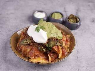 A loaded plate of beef nachos topped with melted cheese, spicy jalapeños, guacamole, sour cream, and fresh cilantro, served with extra dips