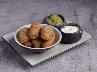 Crispy breaded jalapeño poppers served in a bowl with creamy dipping sauces, including guacamole and sour cream, on a rustic plate