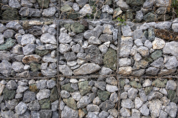 gabion wall, showcasing the texture of the grey stones and the wire mesh. The image highlights the detailed pattern and rugged nature