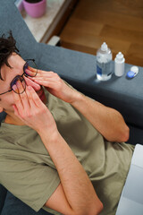 Obraz premium Eye tiredness from working remotely at home. Tired IT specialist with headache in front of laptop.