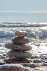 Pebble tower on sunny beach sea wave splashing water balance pyramid harmony equilibrium peace of mind. Cobblestone formation construction seaside