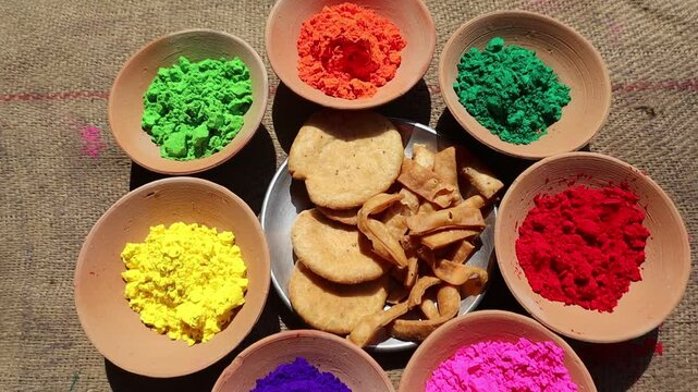 Holi festival setup with vibrant colors in clay bowls and a plate of mathri, a traditional festive snack, symbolizing the joy and culture of Holi celebrations