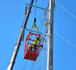 Men in work clothes and hard hats are installing high-voltage wires on a power pole
