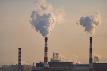 Smoke billowing from industrial chimneys against a vibrant sunset sky creates a striking scene...