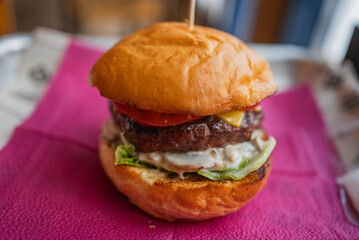 Close-up of a juicy cheeseburger featuring a toasted bun, grilled patty, melted cheese, fresh tomato, crisp lettuce, and creamy mushroom sauce, served on a vibrant pink napkin