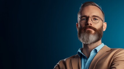 Obraz premium Man with a beard and glasses stands in front of a blue background. He is wearing a suit and a blue shirt