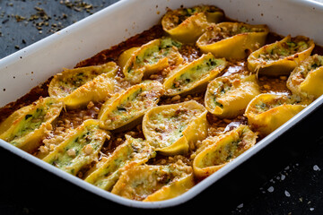 Pasta shells stuffed with cheese and spinach with tomato sauce in baking dish on black table