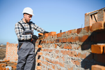 construction mason worker bricklayer installing red brick with trowel putty knife outdoors