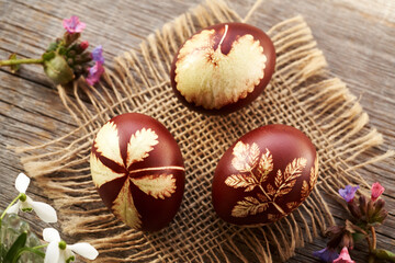 Brown Easter egg dyed with onion peels with a pattern of fresh leaves with spring flowers