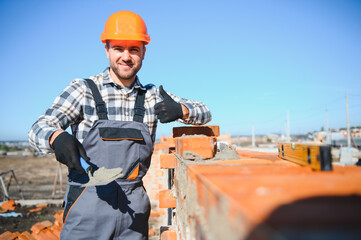 construction mason worker bricklayer installing red brick with trowel putty knife outdoors