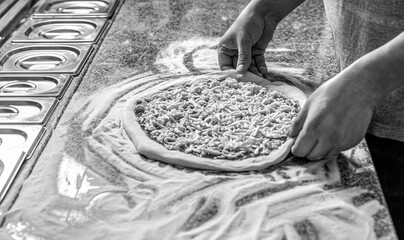 Cooking concept - cook hand adding grated cheese to pizza at pizzeria. Black and white