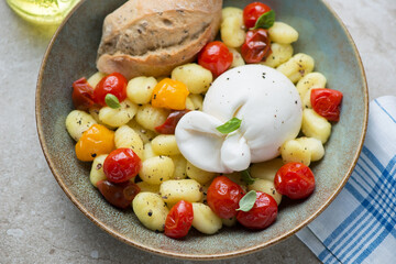 Italian gnocchi with burrata cheese and roasted cherry tomatoes in a rustic plate, horizontal shot, middle close-up