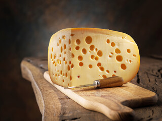 Block of Emmental cheese on wooden cutting board on table.