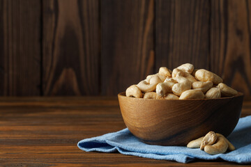 Cashew nuts are piled in bowl placed on blue napkin and rustic wooden table, creating an enticing...