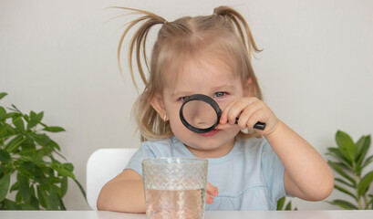 Child examines and examines water under a magnifying glass. Selective focus