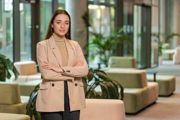 Confident smiling female chief boss in formal clothing looking at the camera. Pretty woman leader office worker looking happy and standing arms crossed in modern office lobby. Businesspeople portraits
