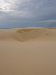 Empty sand dune with cloudy overcast sky.