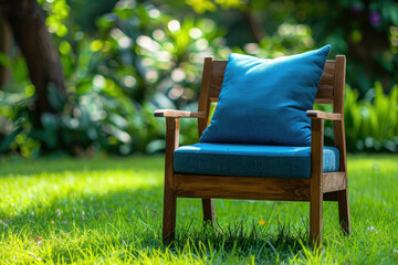 Fototapeta premium A garden armchair featuring a blue pillow, placed on vibrant green grass, surrounded by colorful foliage in a serene outdoor space