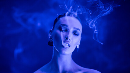 Fashion art portrait of beauty lady with dark makeup and colorful smoke, woman inhaling from an...