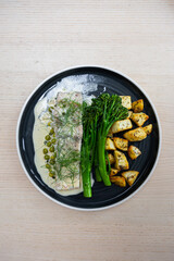 A plate of barramundi with butter sauce, broccolini, and potato.