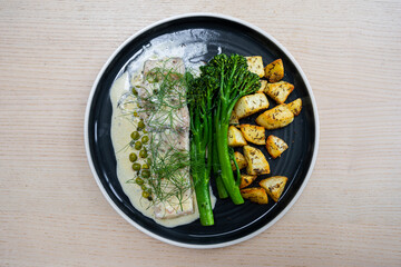 A plate of barramundi with butter sauce, broccolini, and potato.