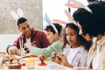Happy family painting easter eggs wearing bunny ears sitting in the kitchen, together having hobby