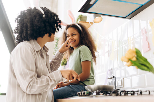 Happy, smiling Latin mother and daughter having fun cooking easter cakes in decorated kitchen