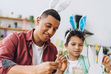 Father and son painting easter bunny decorations wearing bunny ears headband