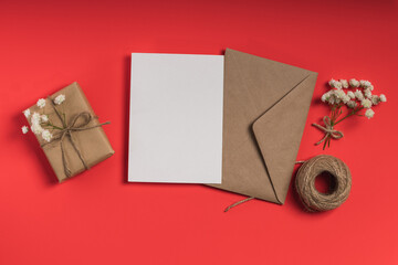 Envelope with blank card, gypsophila and gift box on red background. Greeting card, invitation...