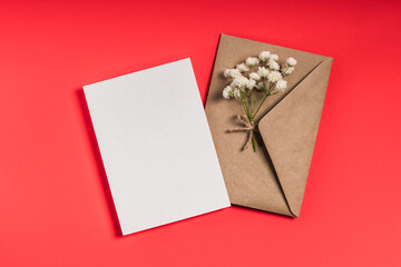 Envelope with blank card and gypsophila on red background. Greeting card, invitation mockup.