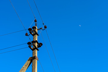 The photograph depicts a concrete electric pole with insulators and wires against a backdrop of...