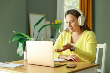 Young woman with headphones working on laptop and discussing the work on a video call