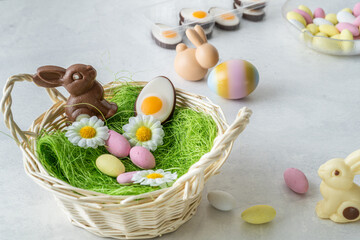 Spring easter basket preparation. Chocolate bunny and pastel colored sweets on white marble stone table. Light and airy, high angle view, copy space
