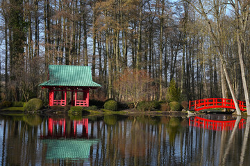 Red gazebo and bridge in Japanese style in the spring garden on the shore of a picturesque lake