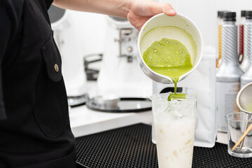 Close up barista hand pouring green tea into a cup.Barista making matcha green tea latte at cozy cafe.Iced tea menu.