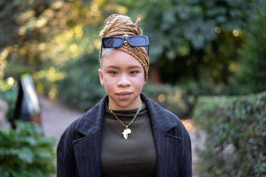 Young albino african american woman wearing Africa shaped necklace and sunglasses is posing in a park