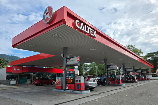 Penang, Malaysia - Mar 9, 2025: A Caltex gas station with fuel pumps under a red canopy, featuring a car parked at the pump and a motorcyclist refueling.