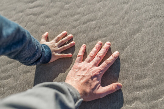 Father and son hands on sand