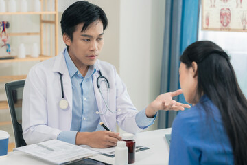 A teenage girl consults with a doctor in a hospital examination room. The doctor records her medical history on a form, giving her advice about her illnesses.
