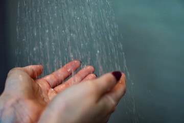Close-up of female hands held open under a stream of falling shower water. The image captures a moment of cleansing, relaxation, and personal care, emphasizing themes like hygiene, wellness, self-care